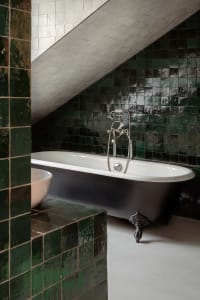 Modern bathroom with a white clawfoot bathtub, green ceramic tiles, and a sloped ceiling.