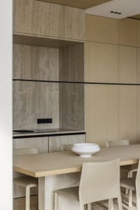 Modern dining room featuring a long table, chairs, and minimalist decor made of concrete and wood materials.
