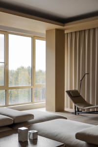A modern minimalist living room featuring a wood floor, light-colored fabric seating, a floor lamp, and large windows with a 
