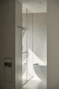 A minimalist bathroom with a freestanding white bathtub, concrete walls, and glass shower enclosure.