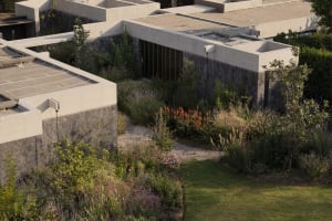 Concrete structures surrounded by a landscaped garden with diverse flora, grass, and stone pathways.