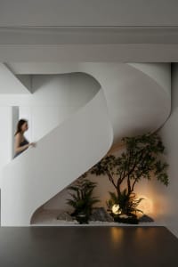 A modern interior featuring a white concrete staircase with a small garden at the bottom.