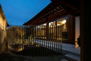 A modern building with wooden exterior at dusk, with illuminated interior visible through large windows.