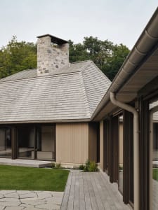 Modern residential exterior with wooden deck, stone chimney, and wooden siding.