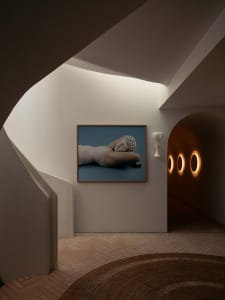 A modern residential hallway with a curved staircase and a framed photograph of a reclining statue on the wall.