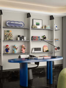 A minimalist home office featuring a blue desk and marble shelving with various decorative items and books.