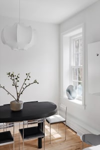 A minimalist dining room featuring a sleek, oval-shaped wooden table with metal legs, accompanied by black and white chairs. 