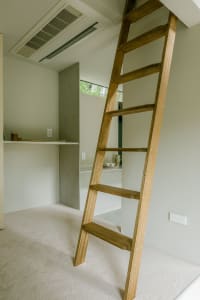 A wooden ladder leaning against a wall, leading up to a higher shelf or storage area.