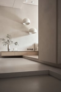 A minimalist living room featuring concrete walls and flooring, with two spherical pendant lights hanging above.