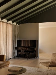 Minimalist living room with a wooden piano, brown leather sofa, and metal-framed armchair.