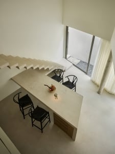 A modern kitchen with a concrete countertop, black chairs, and a bowl of fruit.