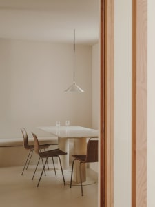 A minimalist dining area with a marble table and wooden chairs against a neutral wall with a wooden beam