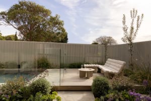 Modern patio featuring wood deck, glass barrier, and greenery.