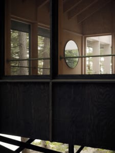 A modern treehouse interior with wooden panels, large windows, and a circular mirror.