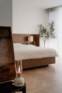 A minimalist bedroom featuring a wooden bed and a large window with sheer curtains.