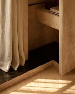 A minimalist interior design featuring a wooden cabinet with a black bottom shelf and a curtain.