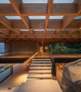 Modern residential interior with wooden beams, concrete stairs, and large windows.