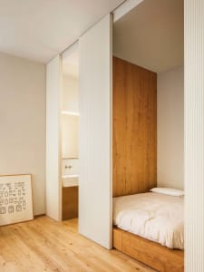 A minimalist bedroom featuring wooden walls and a bed with a wooden frame and white bedding.