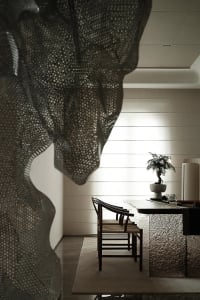 A modern dining room with a textured fabric screen, wooden chairs, and a bonsai tree on a polished dining table.