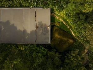 Aerial view of a modern landscape featuring a metal-roofed structure surrounded by lush greenery and a large rock formation.