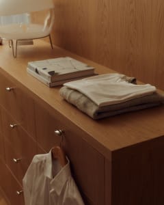 A modern wooden clothing storage unit with clothes, a book, and a shirt.