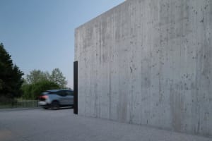 A modern concrete building exterior with a car driving by at dusk.