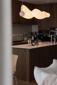 Modern kitchen with wooden finishes and a contemporary light fixture.