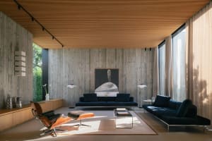 A modern living room featuring a dark blue sofa, floor-to-ceiling windows, and a wooden ceiling and floor.