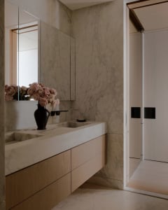 Modern minimalist bathroom featuring marble walls and flooring, with a floating sink and floral arrangement.