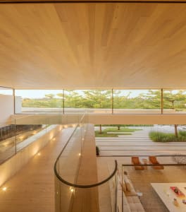 A modern living room with wooden floors, glass walls, and large windows overlooking greenery.