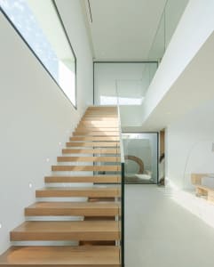Modern staircase featuring wood steps, glass balustrade, and concrete floor.