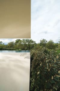 Modern concrete exterior featuring a pool surrounded by lush greenery and a sky view.