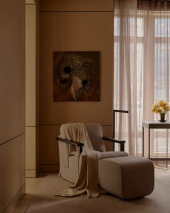 A cozy modern living room with a beige armchair, matching ottoman, and fabric drapes.