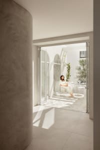 A modern interior with light concrete walls and a woman sitting on a chair in a bright, spacious room.