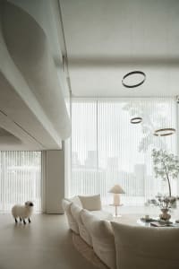 A modern living room with textured fabric sofas, blue pendant lights, and large windows.