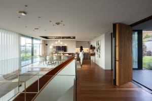A modern residential interior with wooden floors, featuring a spacious living area with large windows, a kitchen, and an open