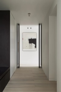 A modern hallway with minimalist black and white decor, featuring abstract art on the wall and dark wooden cabinets.