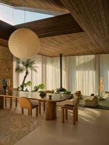 Modern minimalist dining room with a wooden table, marble top, and leather chairs, featuring large windows and a ceiling ligh