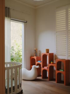 A modern children's bedroom featuring white furniture with bird-shaped armé and orange modular shelving units with children's