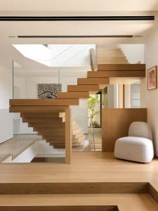 Modern interior design featuring wooden stairs with glass railings and a white chair.