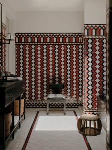 A Victorian-style bathroom with decorative ceramic tiles, a black vanity, and minimalist seating.