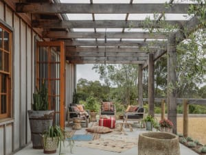 Rustic outdoor living room with wooden pergola, fabric seating, and stone accents.