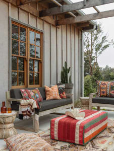 Rustic outdoor living space featuring wooden furniture, fabric cushions, concrete flooring, and metal accents.
