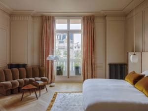 A modern bedroom with a large window, comfortable seating area, and a cozy bed.