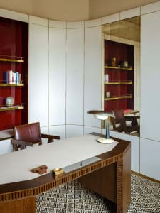 A modern office space featuring a wooden desk, leather chair, and metal accessories.
