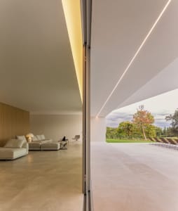 A modern minimalist living room featuring floor-to-ceiling windows, concrete flooring, and wooden walls.
