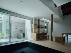 A modern living room with a concrete ceiling and floor, featuring a mid-century modern sofa, a kitchen island with a round wo