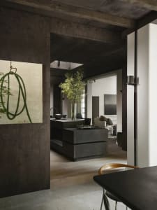 A modern industrial residential interior featuring a concrete kitchen island and wooden dining table with a dark wood floor.