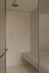 A minimalist bathroom with marble walls and floor, featuring a shower with a built-in bench seat.