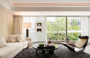 Modern, minimalist living room with white sofa, metal chair, and glass coffee table.
